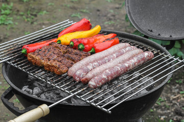 Raw sausages, cutlets and peppers on the grill grate.