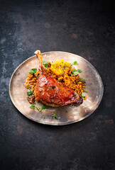 Traditional barbecue gourmet duck haunch with mushroom risotto and orange slices served with spicy chili sauce as close-up on a rustic design plate