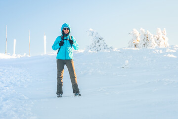 Hruby Jesenik, Young woman hikes on mountain snowy trail, stands on white snow over peak and looks at snowy mountain, winter landscape in mountains on sunny day.