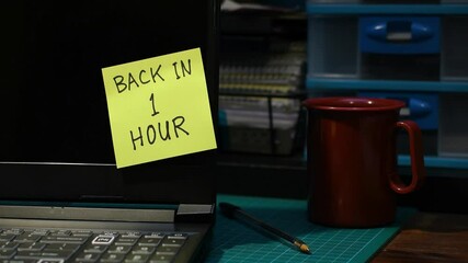 Office setting man’s hand sticking yellow Back in 1 hour note message to laptop mood lighting copy space 