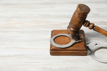 Handcuffs and judge's gavel on white wooden table. Space for text