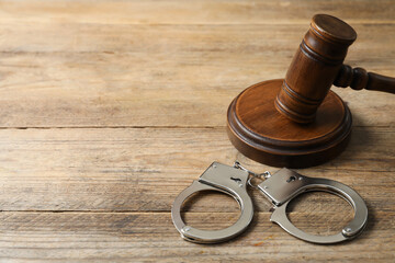 Handcuffs and judge's gavel on wooden table, space for text