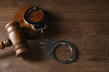 Handcuffs and judge's gavel on wooden table, space for text