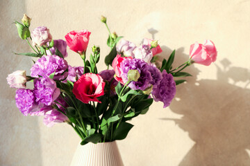 Vase with beautiful eustoma flowers near beige wall, closeup