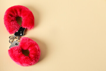 Pink fluffy handcuffs on pale yellow background, top view. Space for text