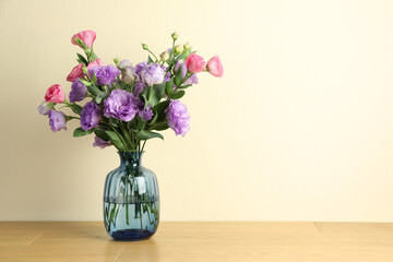 Vase with beautiful eustoma flowers on wooden table, space for text