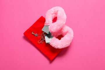 Fluffy handcuffs, key and bag on pink background, top view