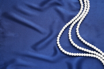 Elegant pearl necklace on dark blue fabric, top view. Space for text