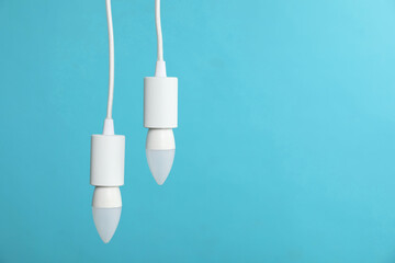 Light bulbs hanging on cords against blue background, space for text