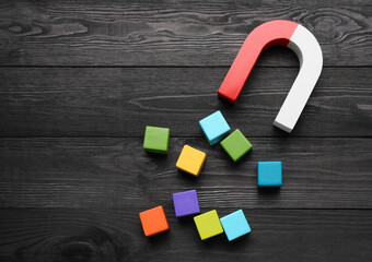 Magnet attracting colorful cubes on wooden table, flat lay. Space for text