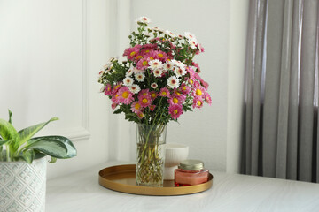 Beautiful flowers in vase and candles on white wooden table at home