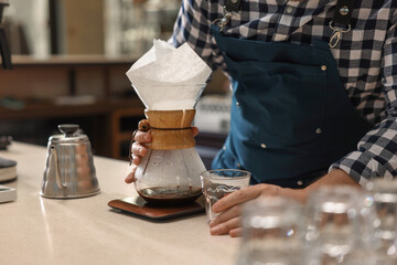 Barista making coffee with glass coffeemaker at table in cafe, closeup