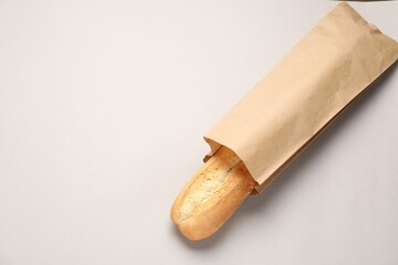 Paper bag with fresh baguette on beige background, top view. Space for text