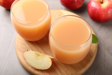 Tasty apple juice in glasses and fresh fruits on grey table, closeup