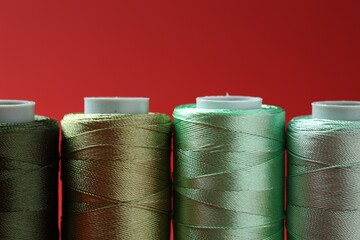 Spools of colorful sewing threads on red background, closeup