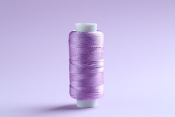Spool of violet sewing thread on lilac background