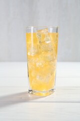 Sweet soda water with ice cubes in glass on white wooden table