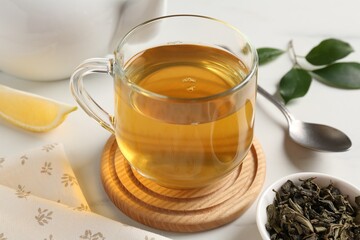 Refreshing green tea in cup and leaves on white table, closeup