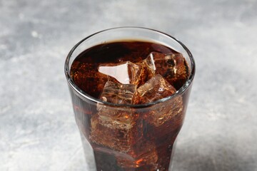 Refreshing cola with ice cubes in glass on light table, closeup