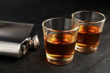 Hip flask and shot glasses of whiskey on black table, closeup