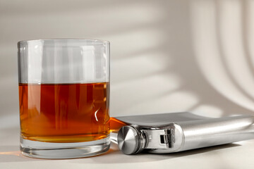 Hip flask and glass of whiskey on light table, closeup
