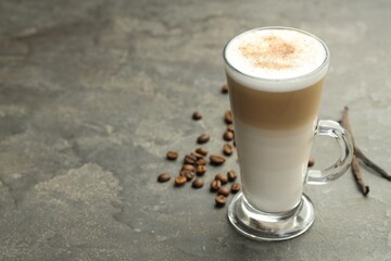 Tasty latte macchiato in glass cup, coffee beans and vanilla pods on grey table, closeup. Space for text
