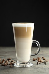 Tasty latte macchiato in glass cup, coffee beans and vanilla pods on grey table, closeup
