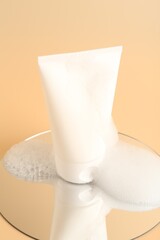 Tube of cosmetic product with foam and mirror on beige background