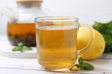 Aromatic mint tea with lemons and fresh leaves on white wooden table, closeup