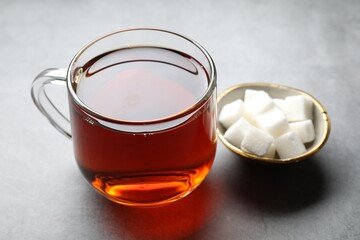 Refreshing black tea in cup and sugar cubes on grey table, closeup