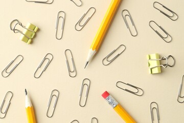 Paper clips and pencils on beige background, flat lay