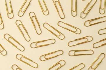 Golden paper clips on beige background, flat lay