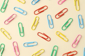 Colorful paper clips on beige background, flat lay