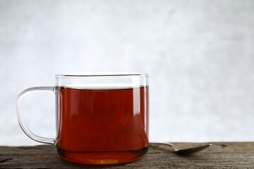 Aromatic black tea in cup and spoon on wooden table, closeup. Space for text