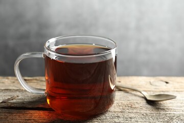 Aromatic black tea in cup and spoon on wooden table, closeup