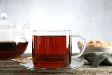 Aromatic black tea in cup and spoon on wooden table, closeup