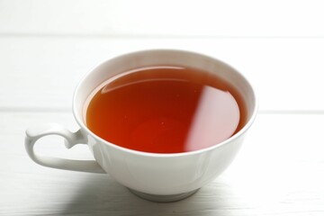 Aromatic black tea in cup on white wooden table, closeup