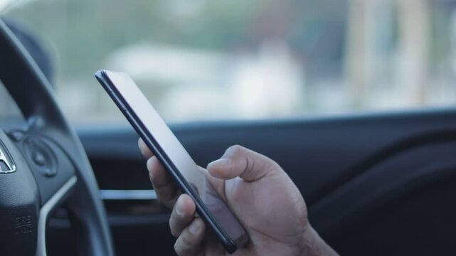 B roll - Closeup of man hand using smartphone while seated comfortably inside a car. A person using a mobile phone to check email for work or text SMS messages. Online business communication concept.