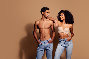 Young couple in studio wearing jeans standing close against beige background