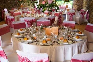This elegant wedding reception table showcases a white tablecloth adorned with a pink and white floral centerpiece, complemented by pink napkins and matching dinnerware.