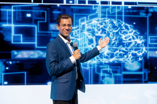 Smiling specialist talking at AI tech summit event gathering professionals seeking to discover latest AI solutions. Happy speaker presents how can AI be leveraged to accelerate innovation