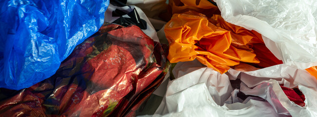 background of too many plastic bags on a domestic household table, harmful to the environment and causing pollution. Sustainability and waste from consumer spending, filling up cupboards in houses © andrew