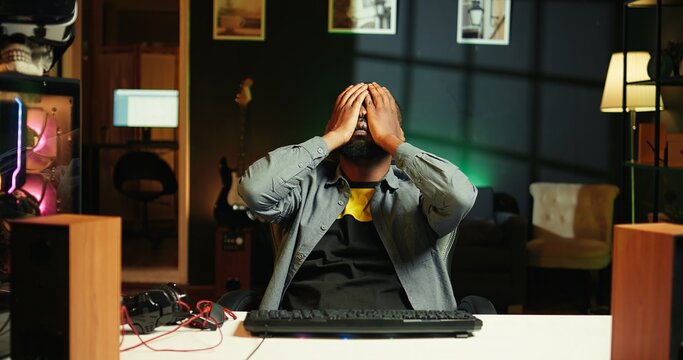 Upset african american man frustrated after losing online competitive multiplayer match playing on cutting edge gaming setup. Gamer feeling sad after being defeated in internet videogame, camera B