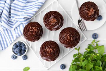 Tasty cupcakes with chocolate cream and blueberries on white tiled table, flat lay