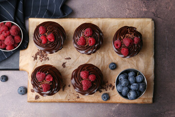 Tasty cupcakes with chocolate cream and berries on brown table, flat lay