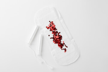 Menstrual pad with red sequins and tampons on white background, top view