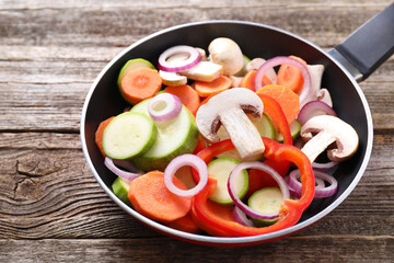 Frying pan with mix of fresh vegetables and mushrooms on wooden table, closeup