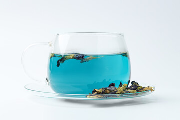 Fresh butterfly pea flower tea in cup and dry petals on white table, closeup
