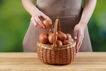 Woman with basket of eggs at wooden table on blurred background, closeup