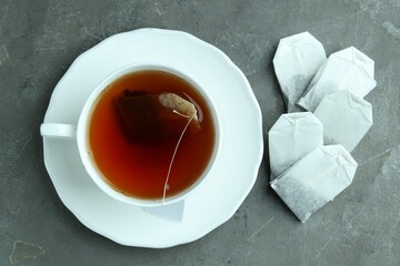Tea bags and cup with hot drink on gray textured table, flat lay